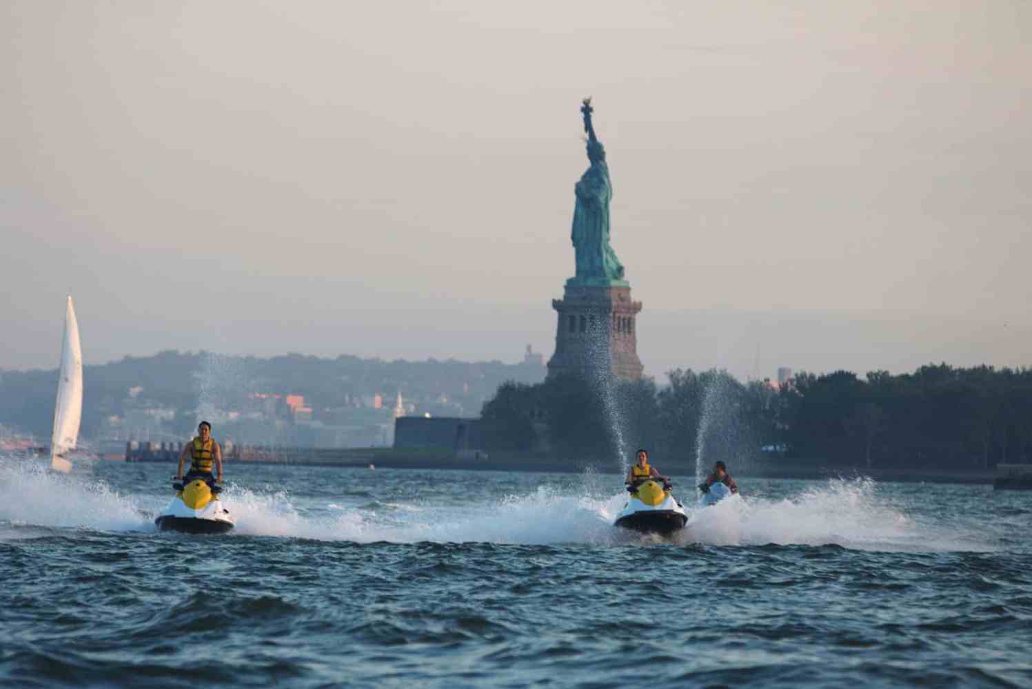 people jet skiing in front of the statue of liberty